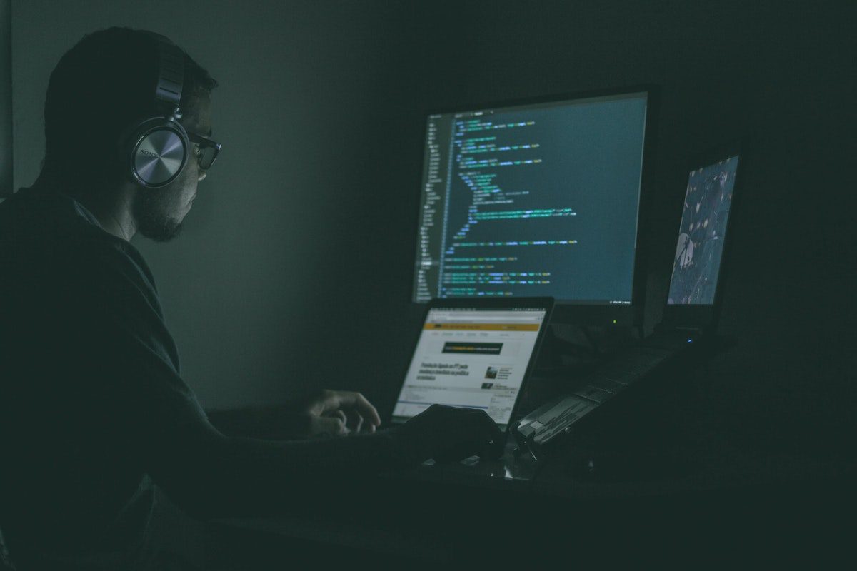 A man sitting in front of a computer screen displaying lines of code. React Remote Jobs