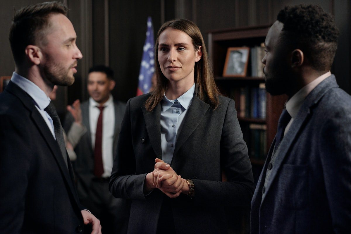 A central suited female lawyer with her hands clasped having a discussion with two suited male lawyers. A Day in the Life of a Lawyer