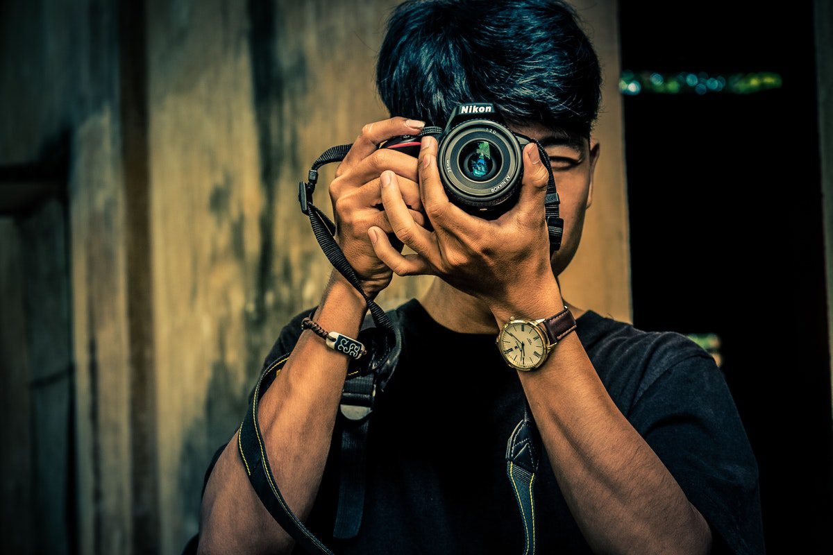 A man holding a camera to his face taking a photo. A Day In The Life Of A Photographer