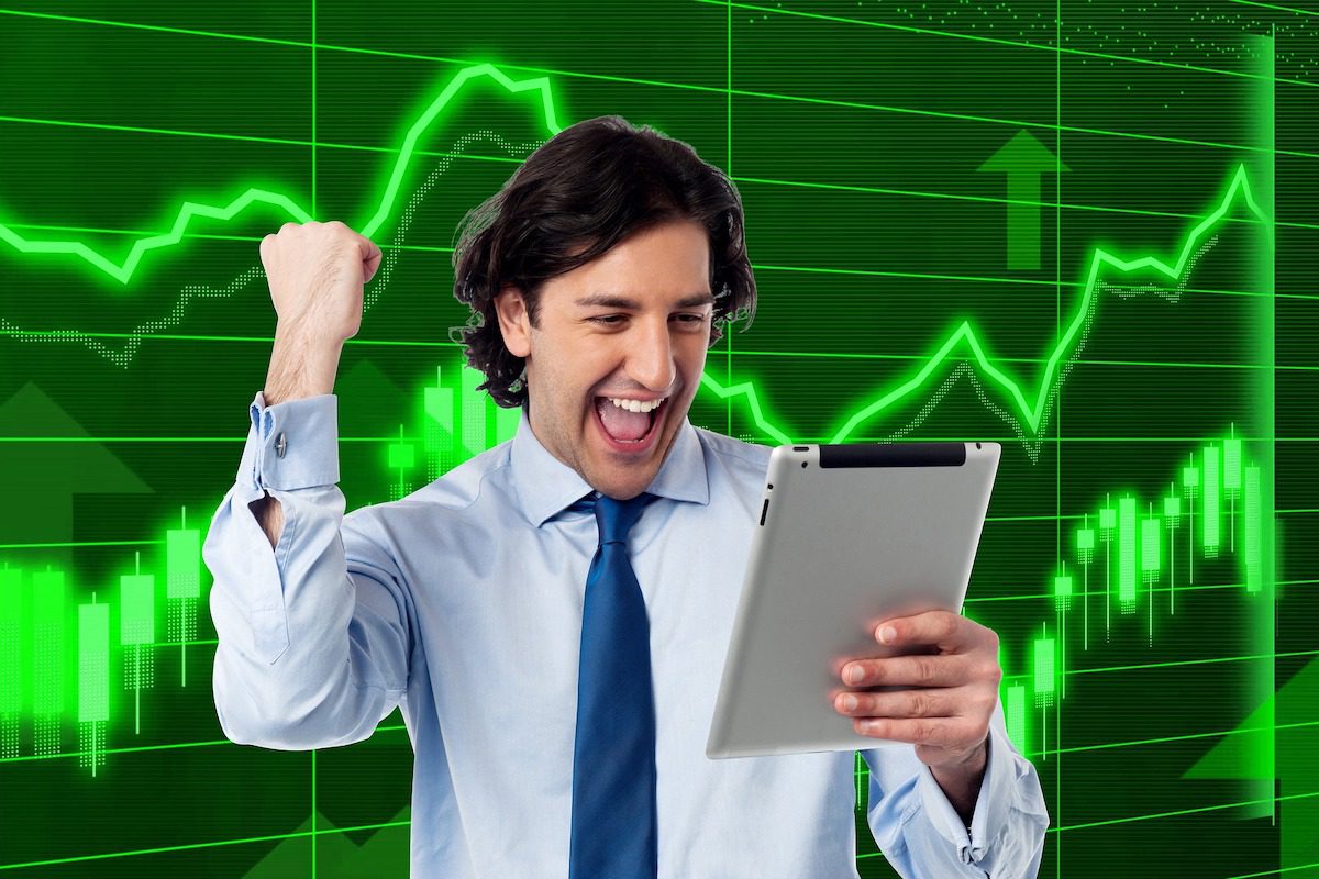 An excited trading manager holding a silver tablet and celebrating a bull market. A Day In The Life Of A Day Trader
