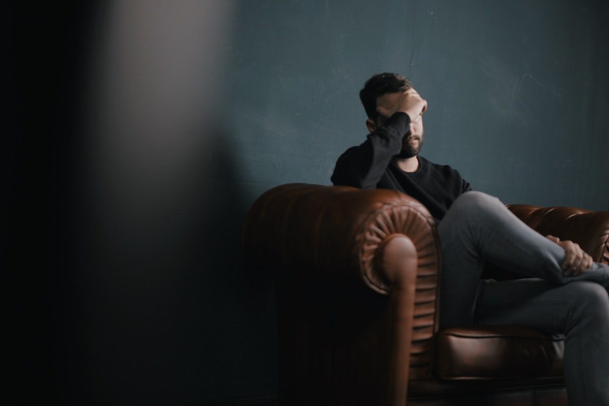 A man sitting on a sofa with his face cast down and his hand on his forehead. A Day In The Life Of A Speech Pathologist