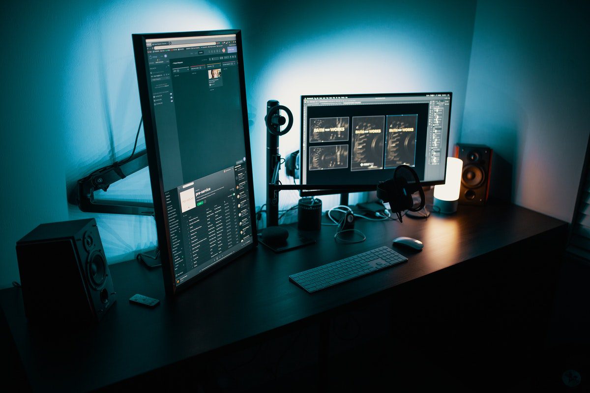 Office setup in a dark room with two computer screens and a keyboard. How Technology Helps Business