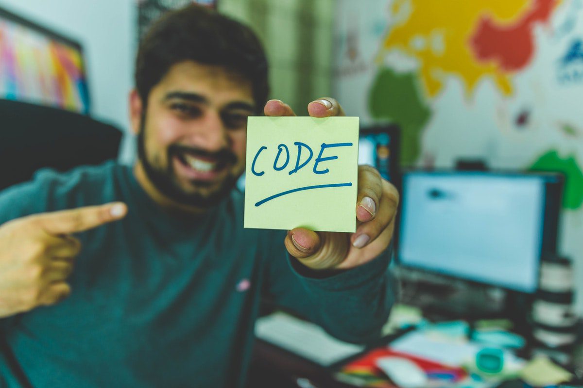 Man in grey sweater holding yellow sticky note that says code. CSS Exercises