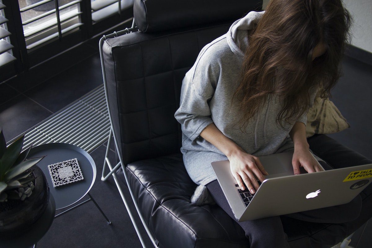 A girl on a black leather chair bent over working on her laptop. Coding Exercises