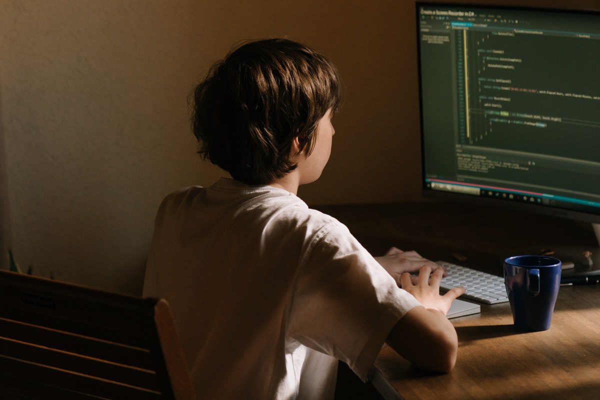 Boy in white shirt sitting on a chair in front of a computer watching Python training videos