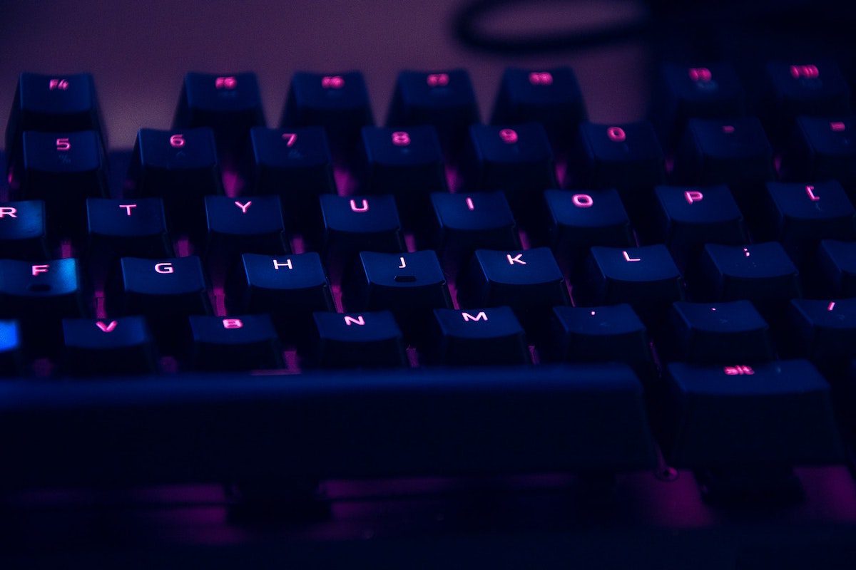 A close-up view of a computer keyboard, lit up in purple.