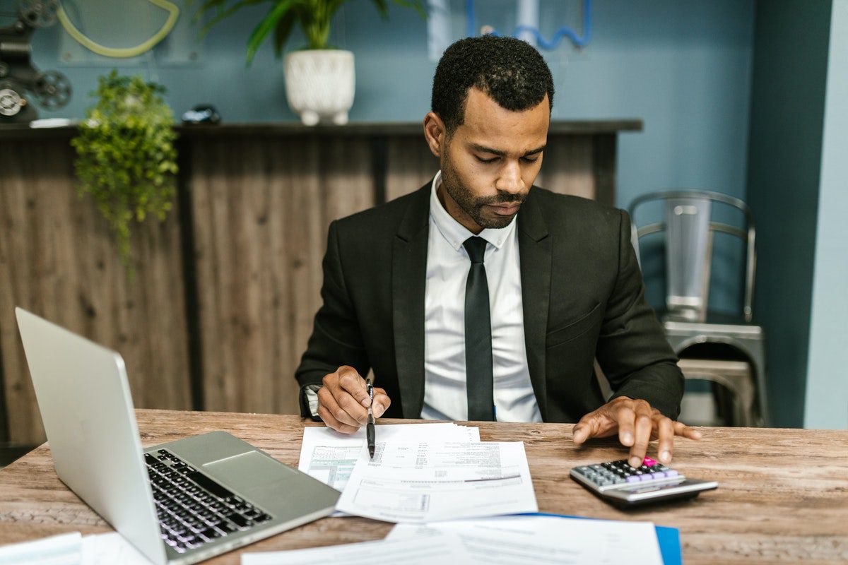 Man in black suit using a calculator and laptop. Jobs That Use Exponential Functions