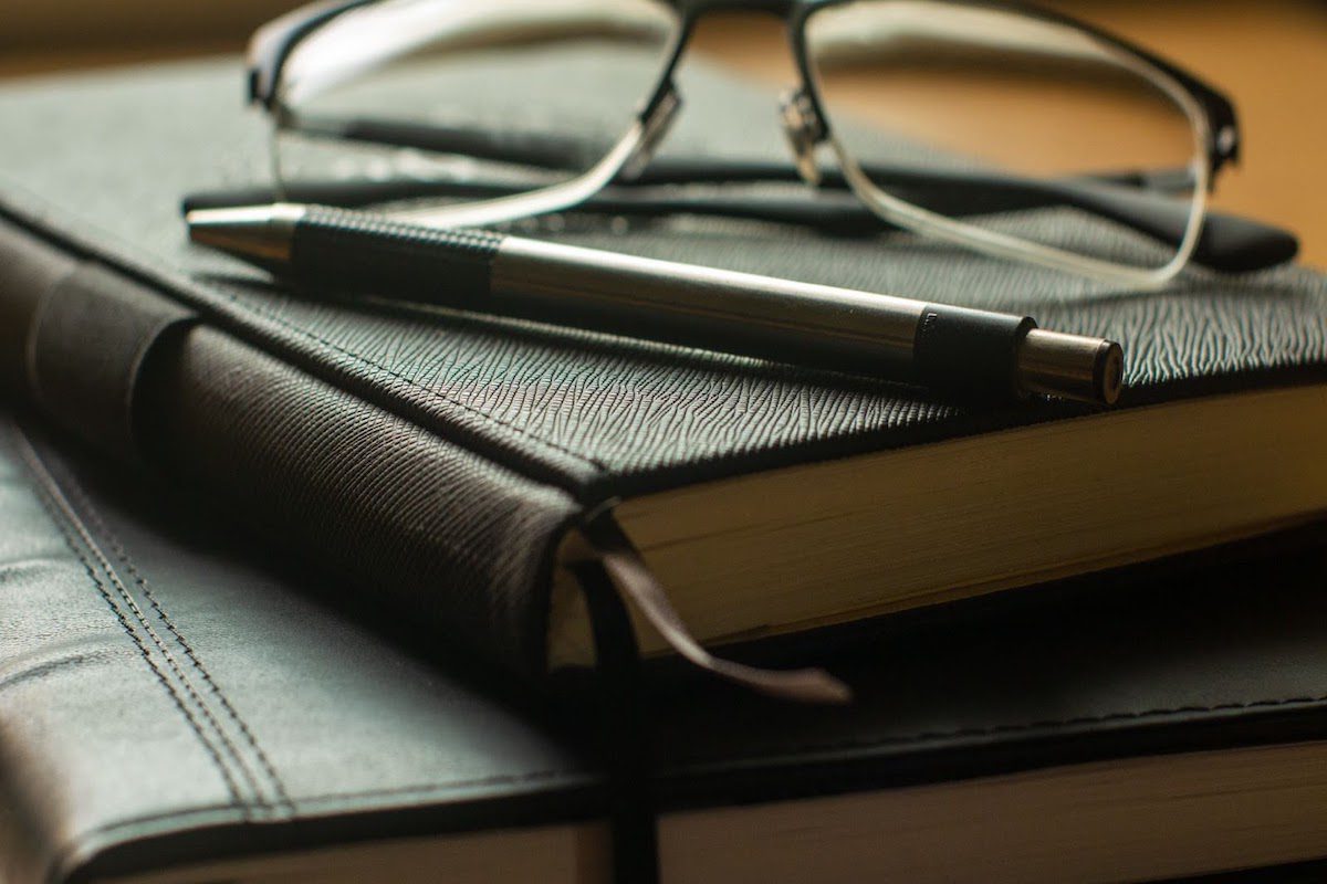 A pen and a pair of reading glasses set on top of a pair of leather-bound journals
