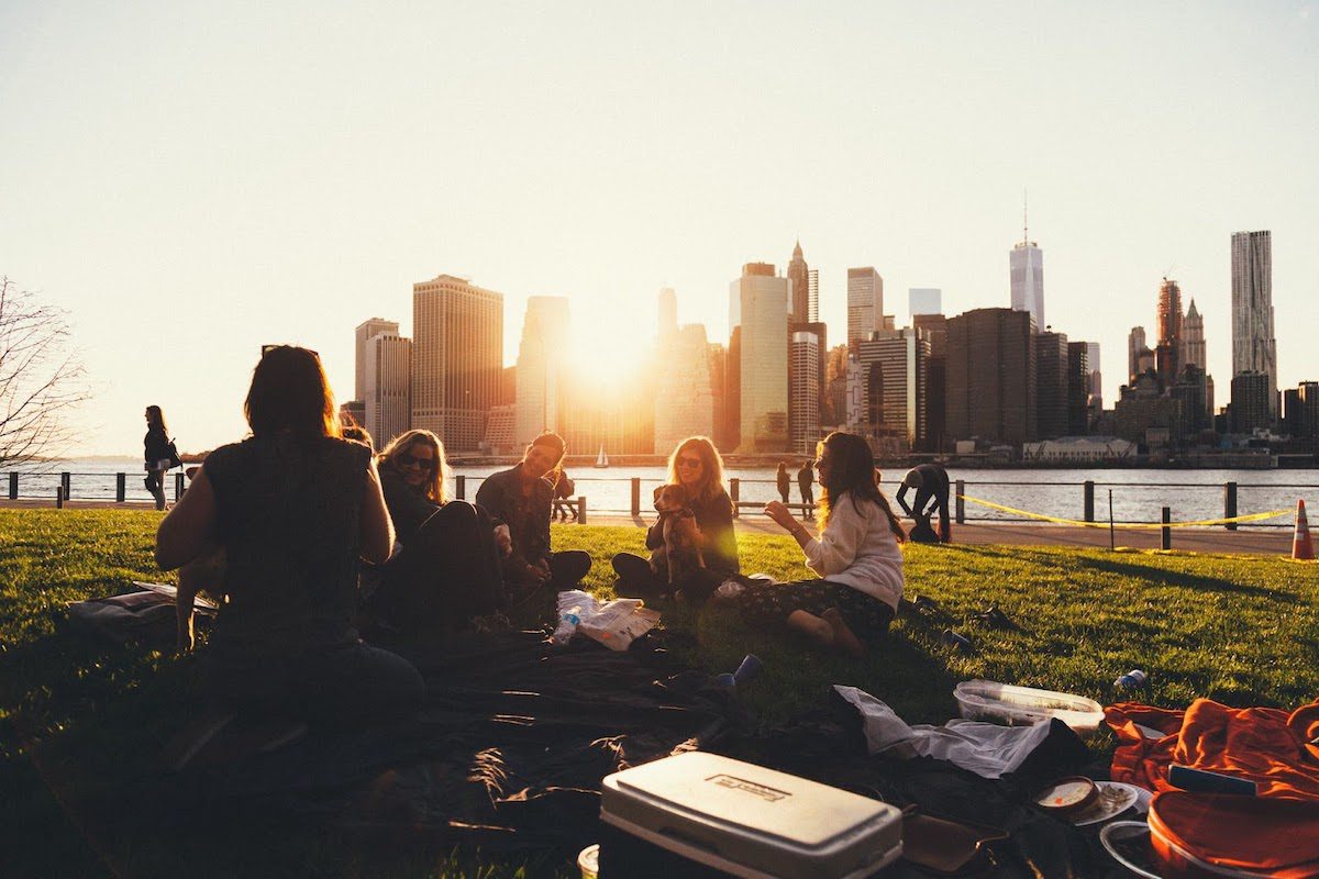A group of community college students sitting in a grassy park with a city skyline in the background.