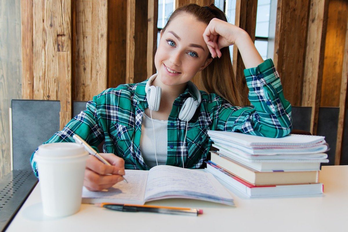 young woman at a desk with books and headphones. Best Podcasts for Young Women