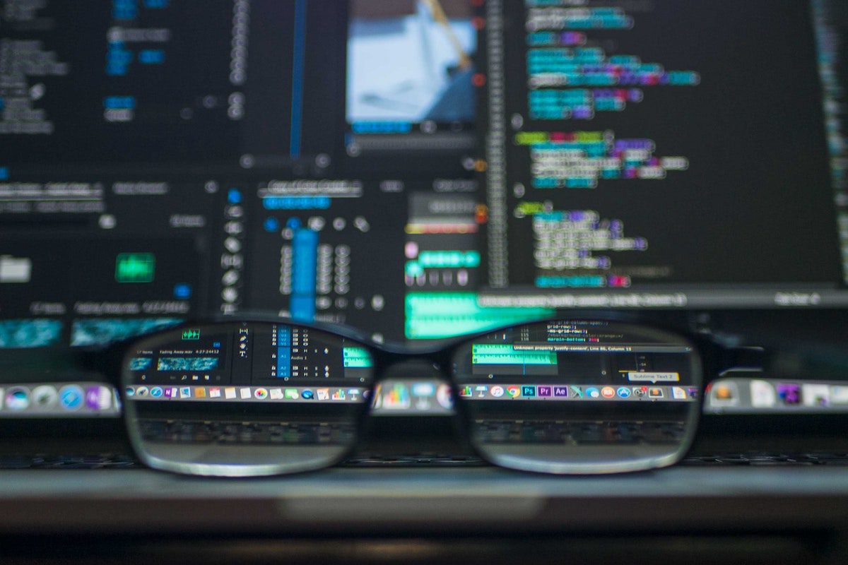 A close-up photo of glasses with a laptop displaying code behind them. Trends In Technology