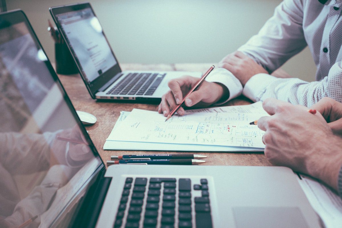 Two accountants sitting at a table with their laptops open, trying to identify trends in a business’ finances. How Does Accounting Help Business