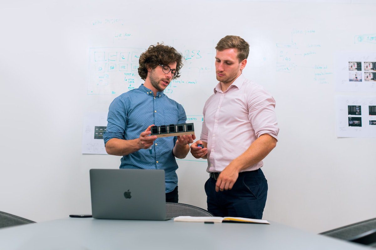 Two professionals discussing a product and standing in front of a laptop. How Data Science Helps Business