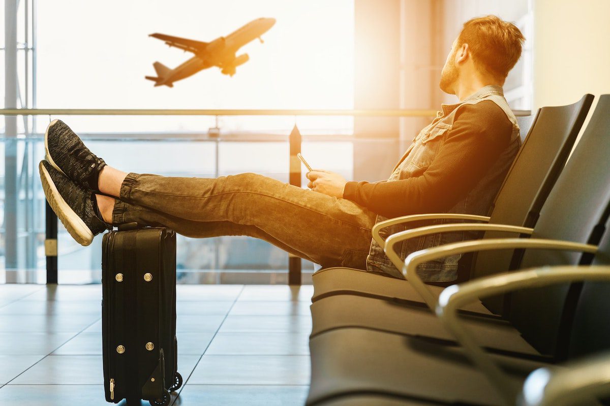 A man sitting on a gang chair and resting his feet on luggage. Jobs That Require Travel