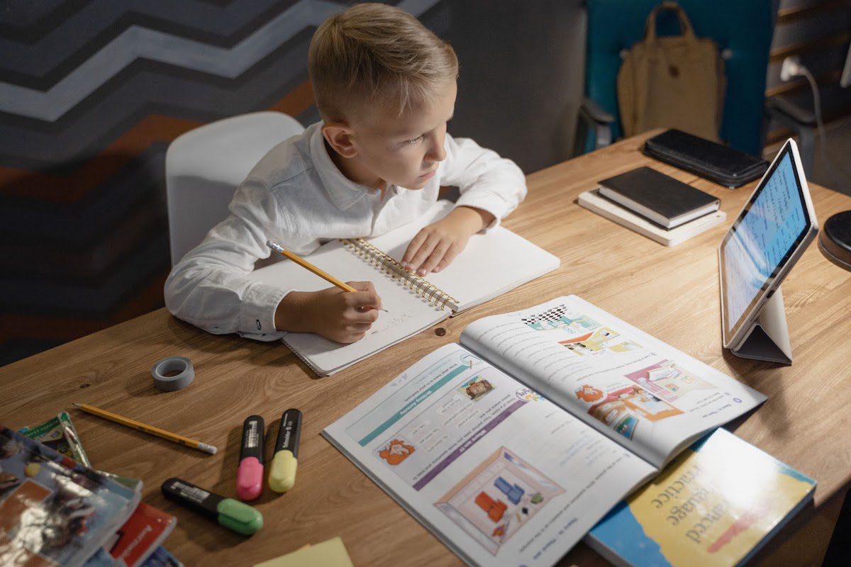  A boy taking notes from an iPad with an opened textbook in front of him Learn Artificial Intelligence For Kids