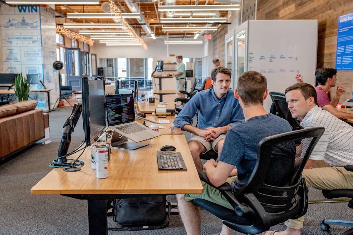 Three men sitting in an office discussing something at a desk with computers on it  How To Make Photos Load Faster On Website