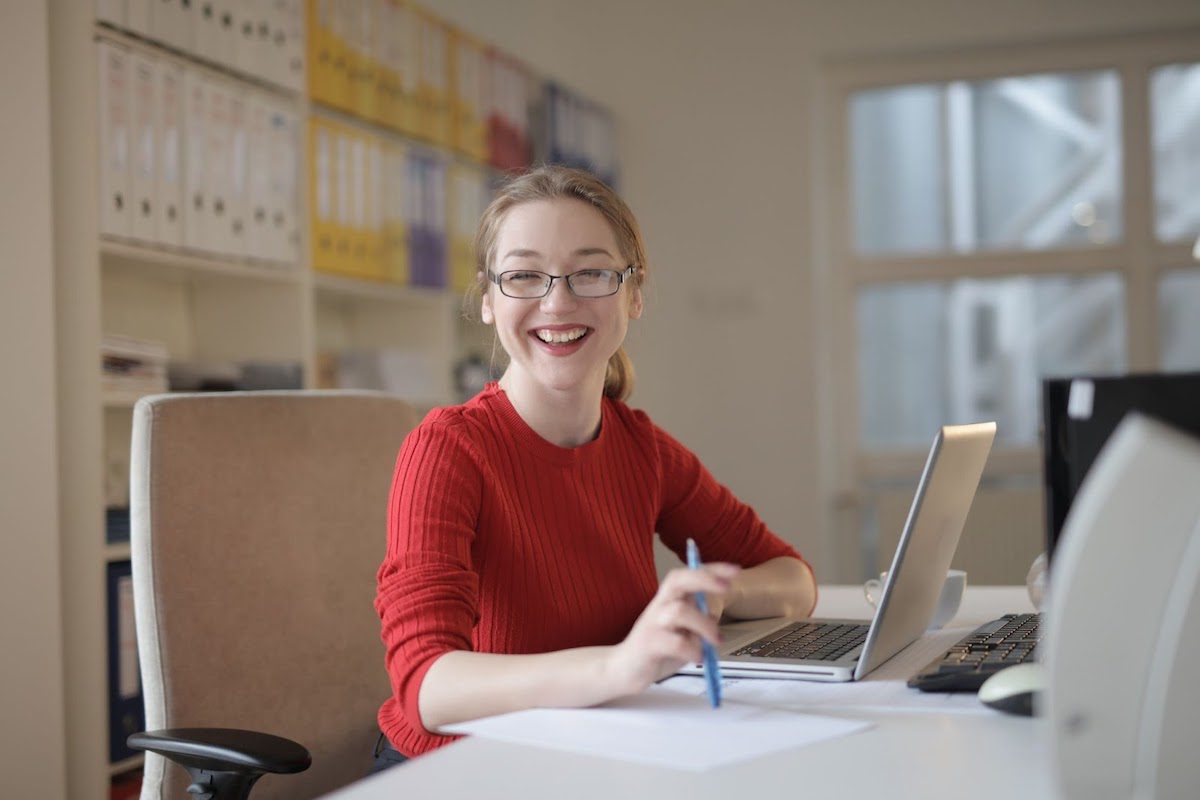 A woman in a red sweater smiling at her desk in an office. How To Get An Internship At Nintendo