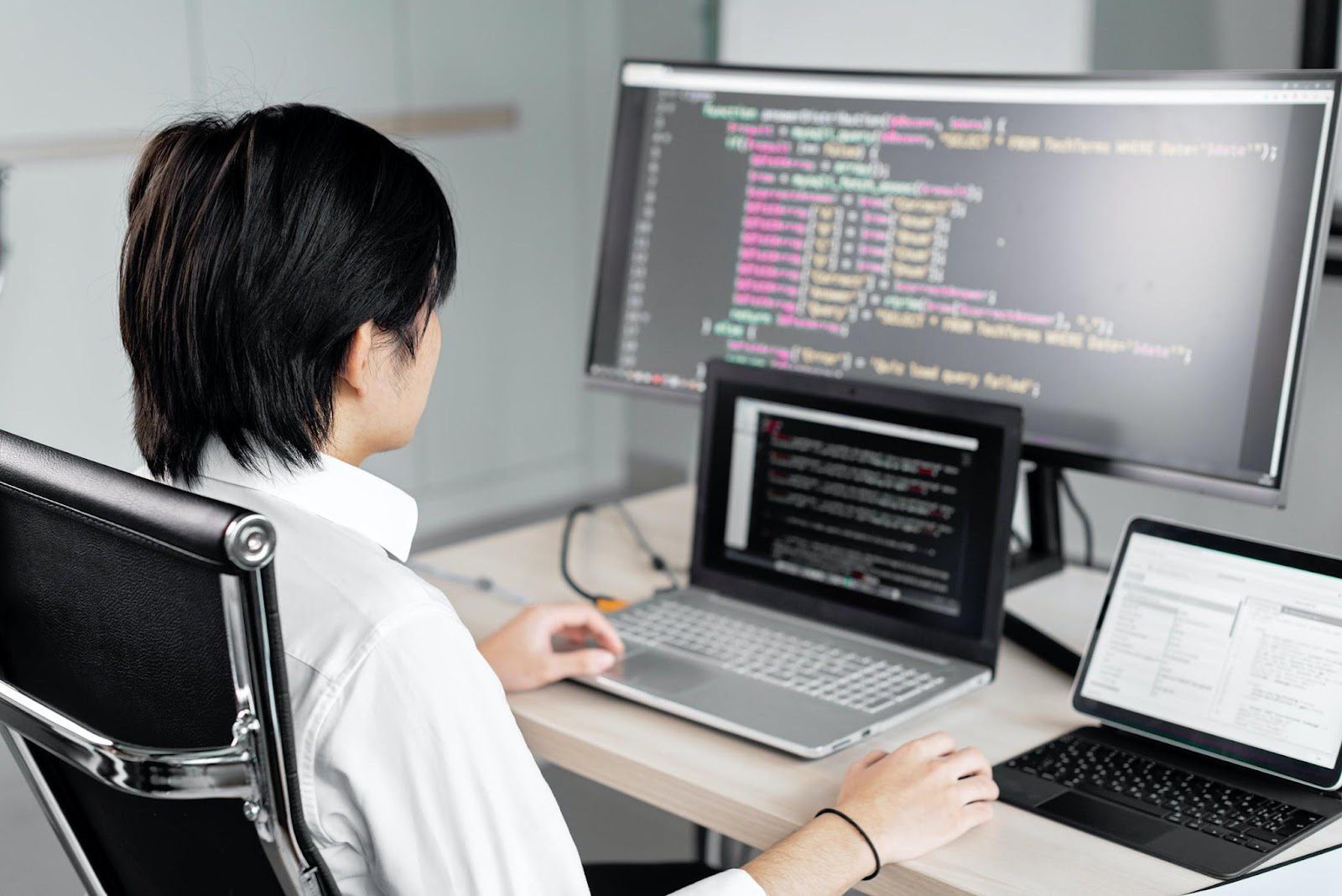 A man sitting at a desk in front of three computers while working on code. Companies That Use Node.js