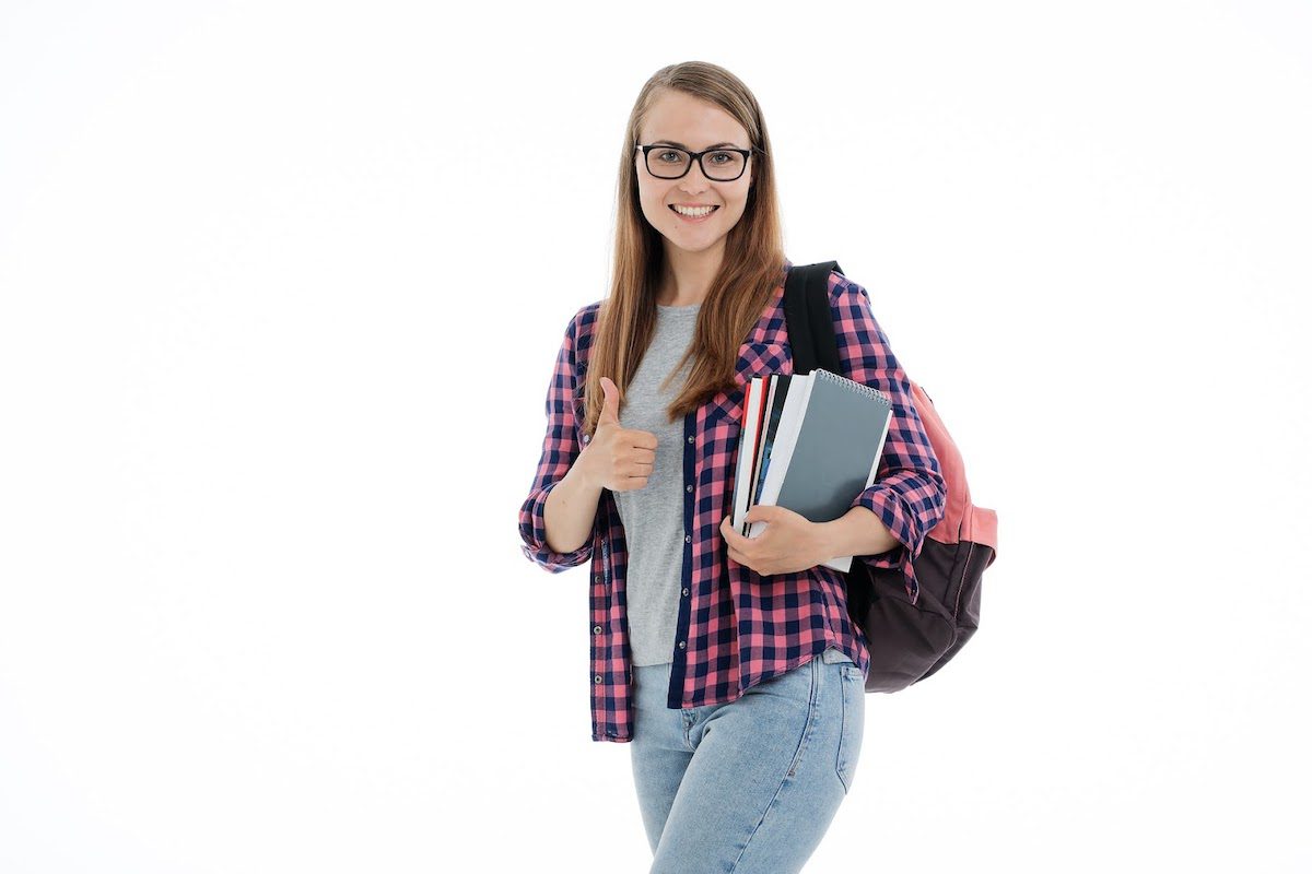 A female student carrying books and giving a thumbs-up. Trends In College Admissions