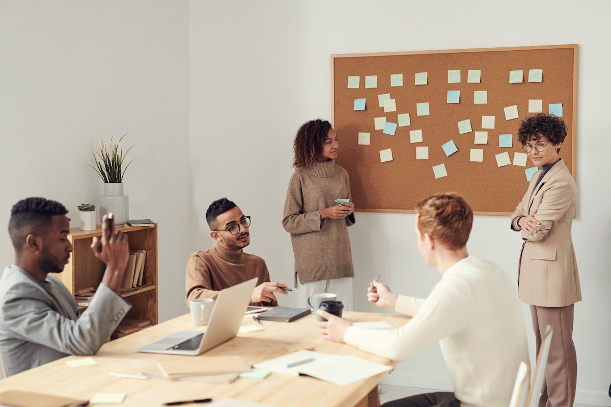 Two people stand in front of a corkboard that has sticky notes on it.   Trends In Diversity