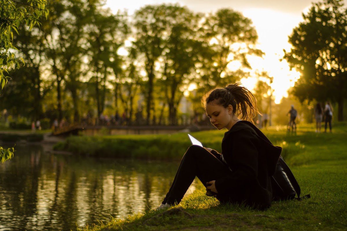 A woman sitting on the grass and reading by the water-side