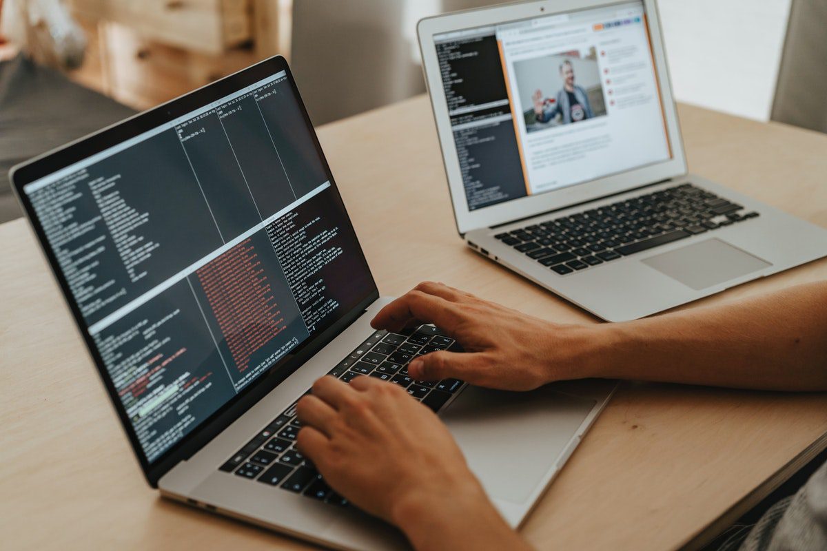 An individual coding on a MacBook with another laptop at his side. Best Programming Languages For Beginners