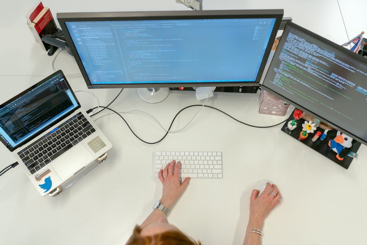 Female programmer coding at her desk using two desktops and a laptop. 