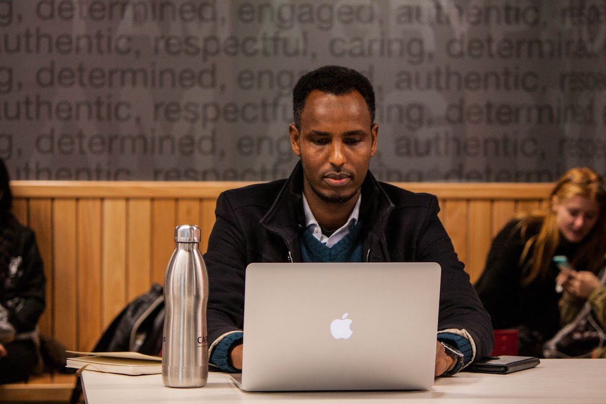  A young man using a silver Macbook at a table. How To Get Into An MBA Program