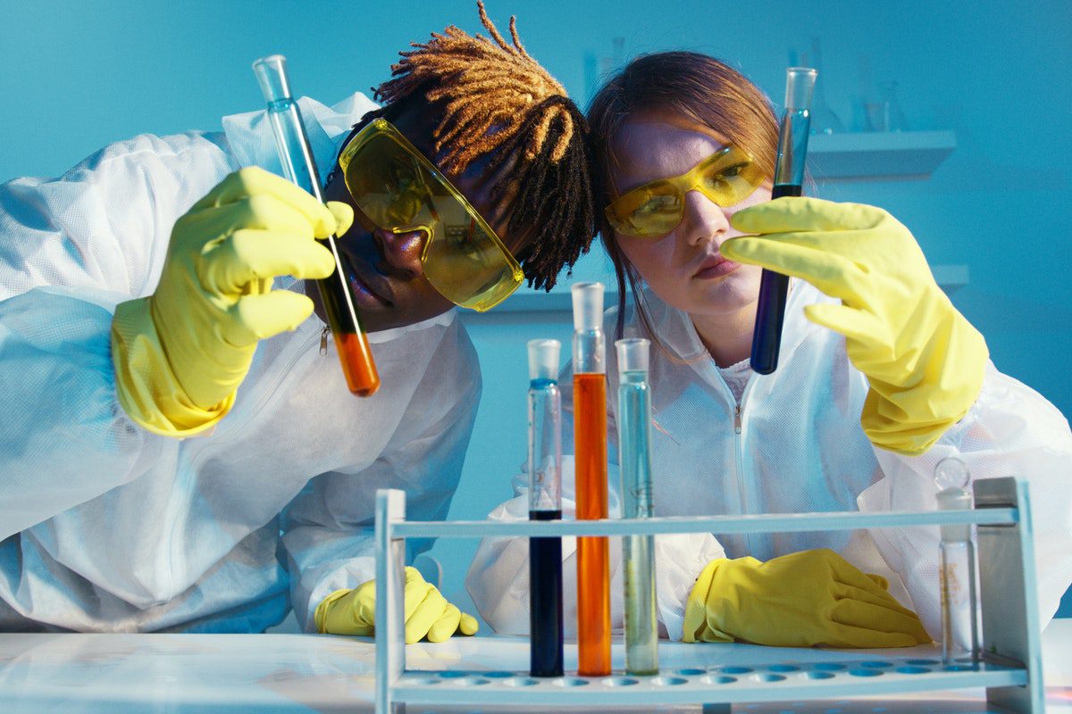 two high school research interns wearing lab safety equipment, holding and looking at test tubes