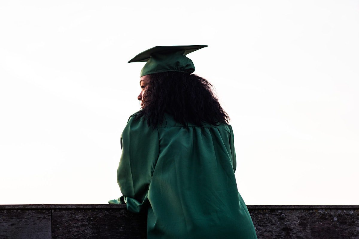 A student wearing a green graduation cap and gown. Financial Aid For Masters Degree