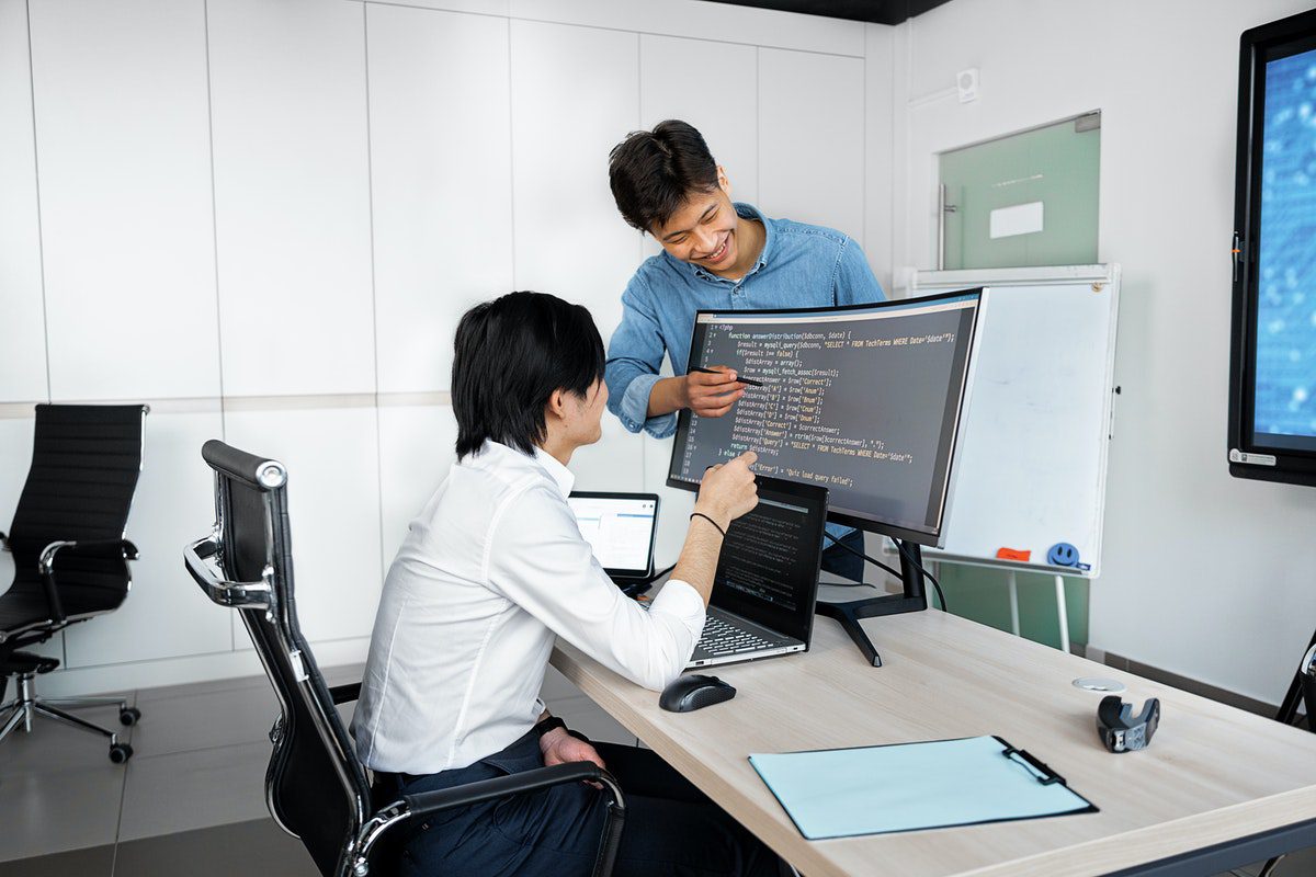 A worker coding at a computer with a manager praising his work.