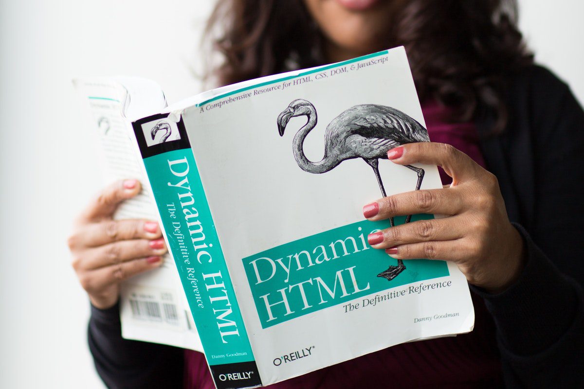 Person reading a book on Dynamic HTML to improve their chances of landing creative jobs without a degree.
