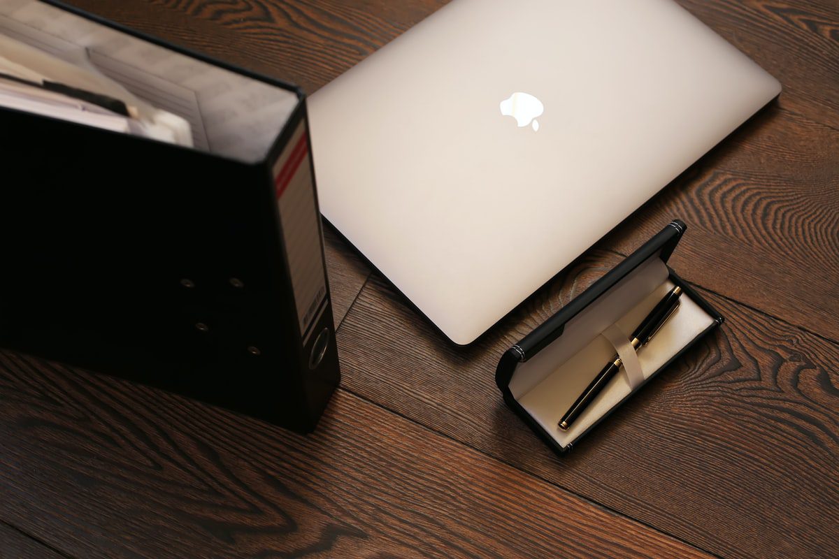 A silver Mac placed next to a physical paper folder on a brown wooden table