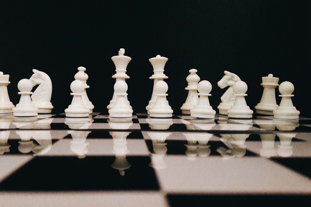 A glass chess board with white chess pieces set up. 
