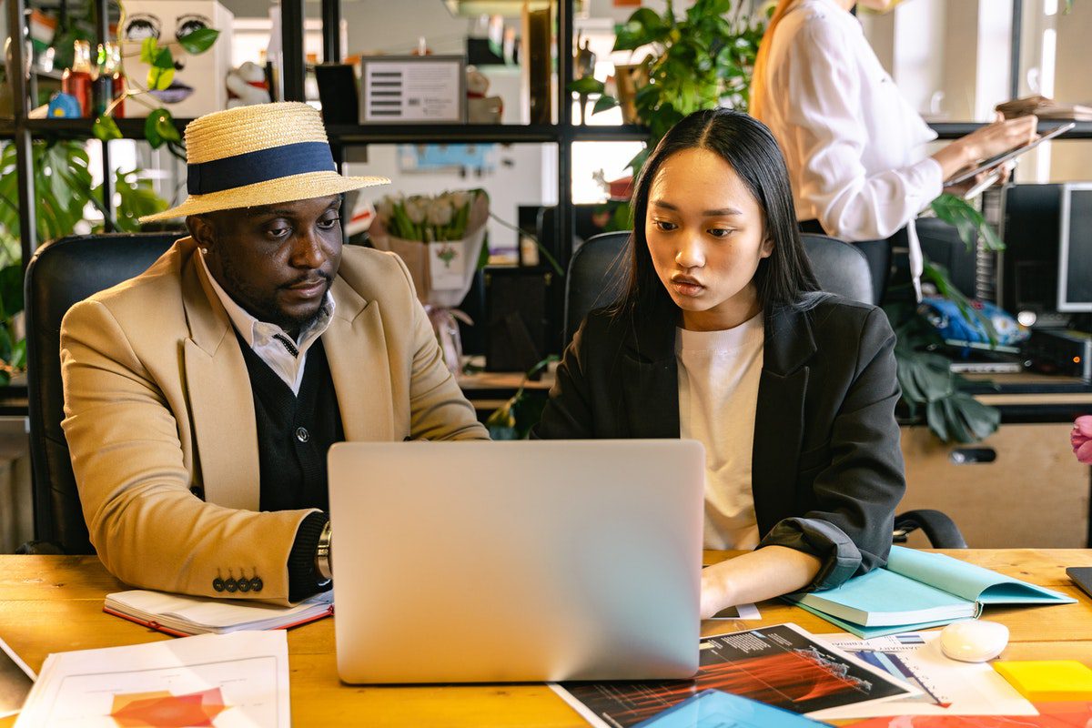 Two people learning to code together at a laptop in an office.