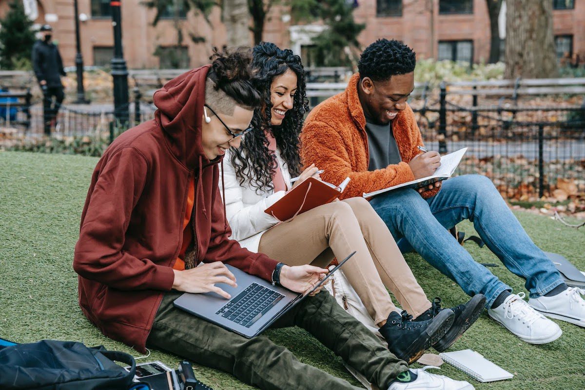Three university students sitting on the grass working