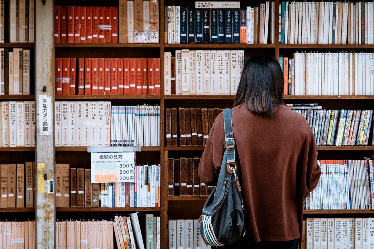 A university student standing in front of a bookcase at the school’s library