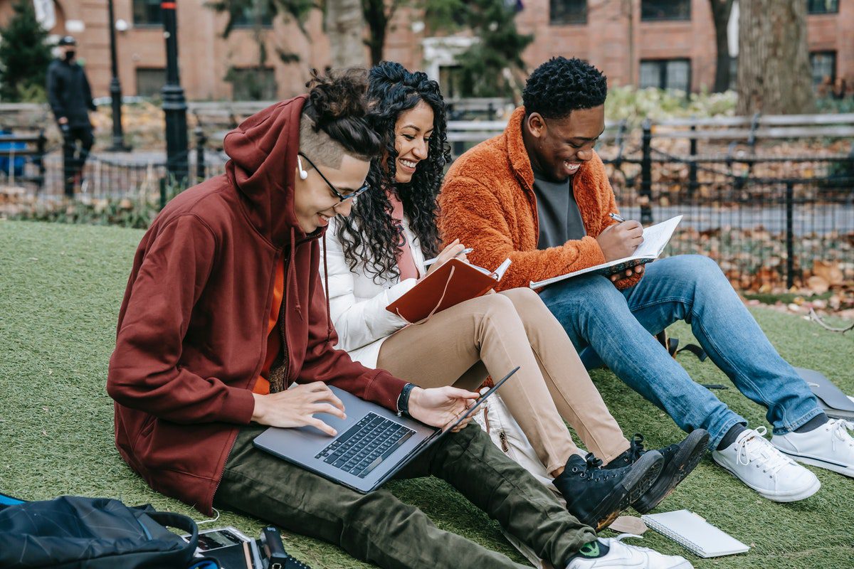 A group of college students sitting on the grass, reading, and talking