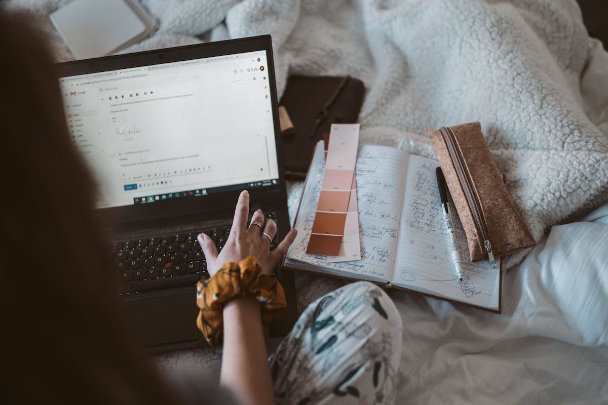 A woman sits on her bed, writing an email on her laptop. How To Write An Email