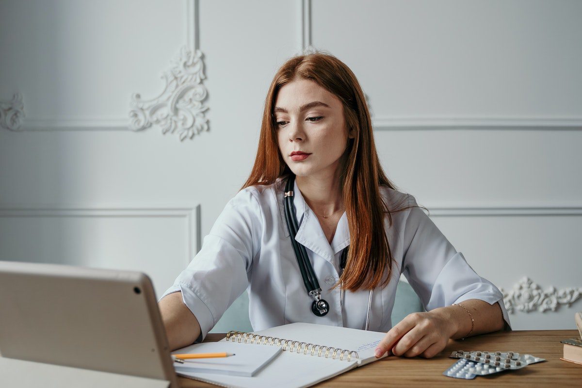 A charge nurse working at her desk with a notepad, pencil, computer, and pill packets. How To Get A Job At Northwell Health