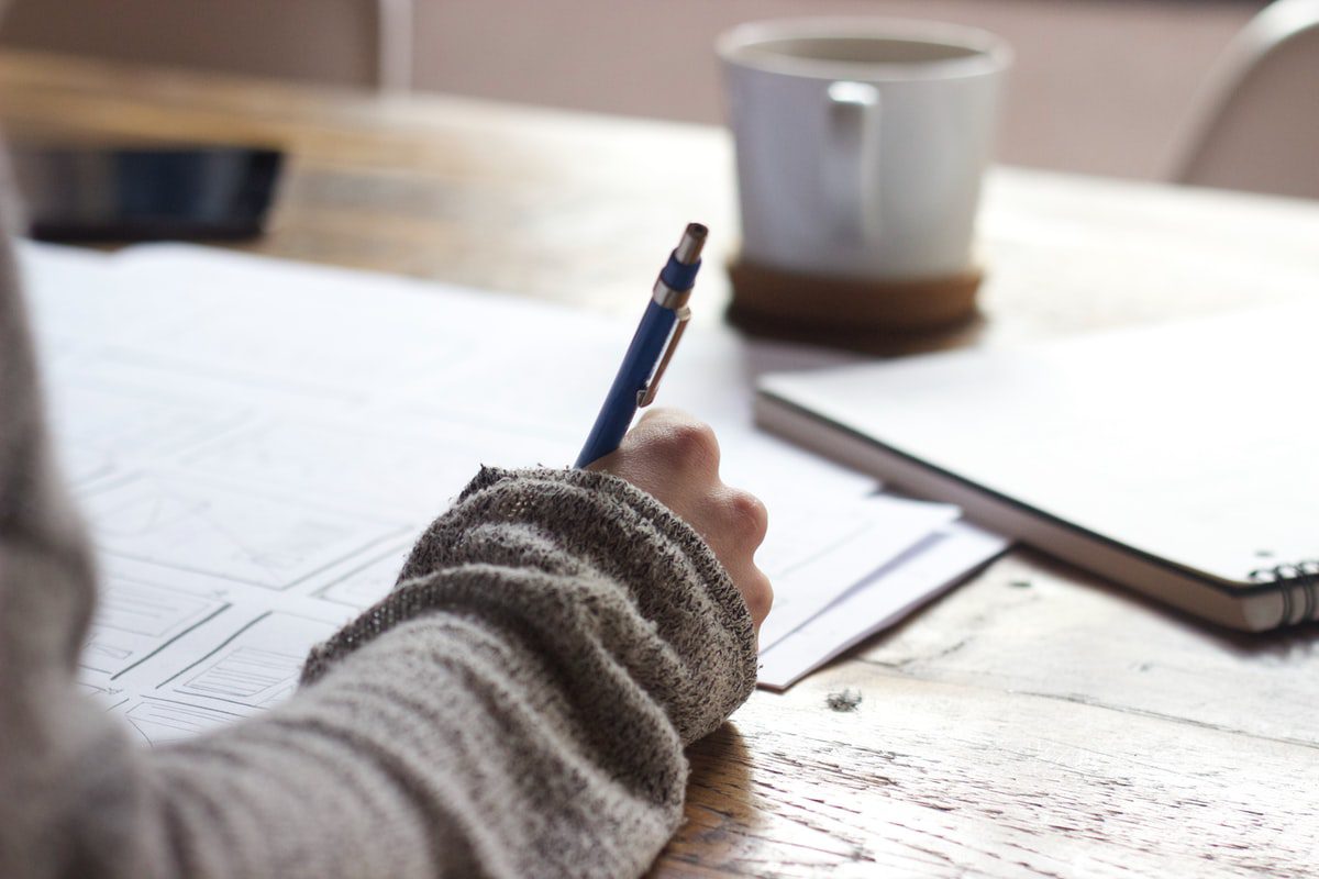 A person writing a letter on a dark brown wooden table