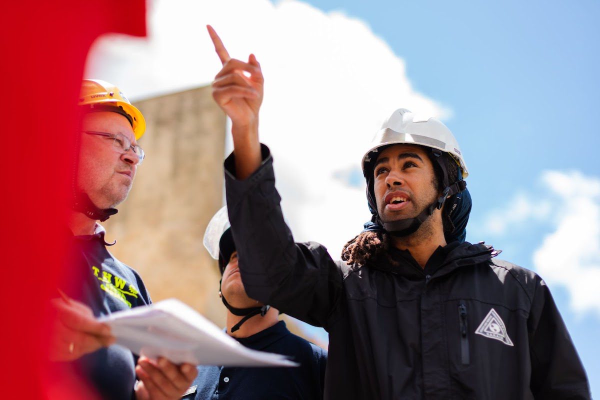 A man at a construction site wearing a hard hat and pointing up