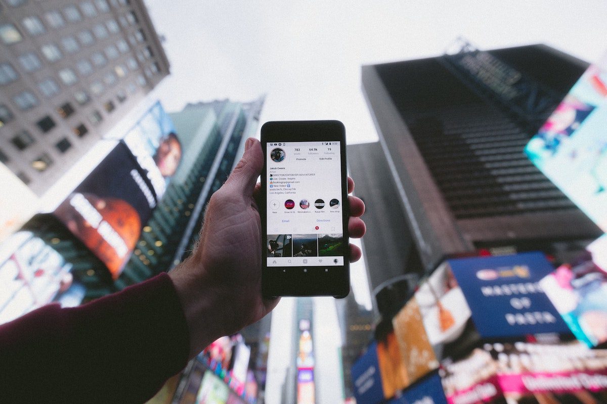 A person holding a smartphone up to the sky, surrounded by skyscrapers, with a social media app open