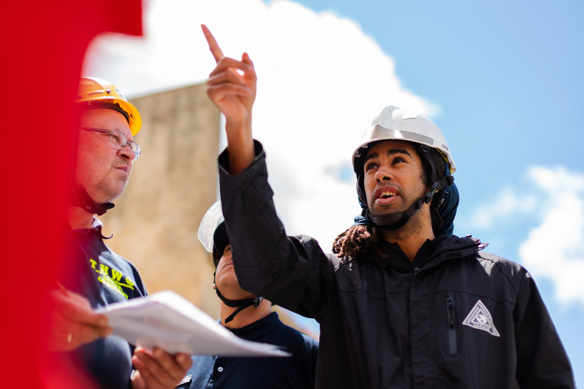 Man with a black jacket and a white helmet pointing upwards while on the engineering site