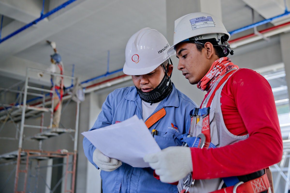 Two manufacturing engineers wearing hard hats and reviewing facilities management plans in a factory.  