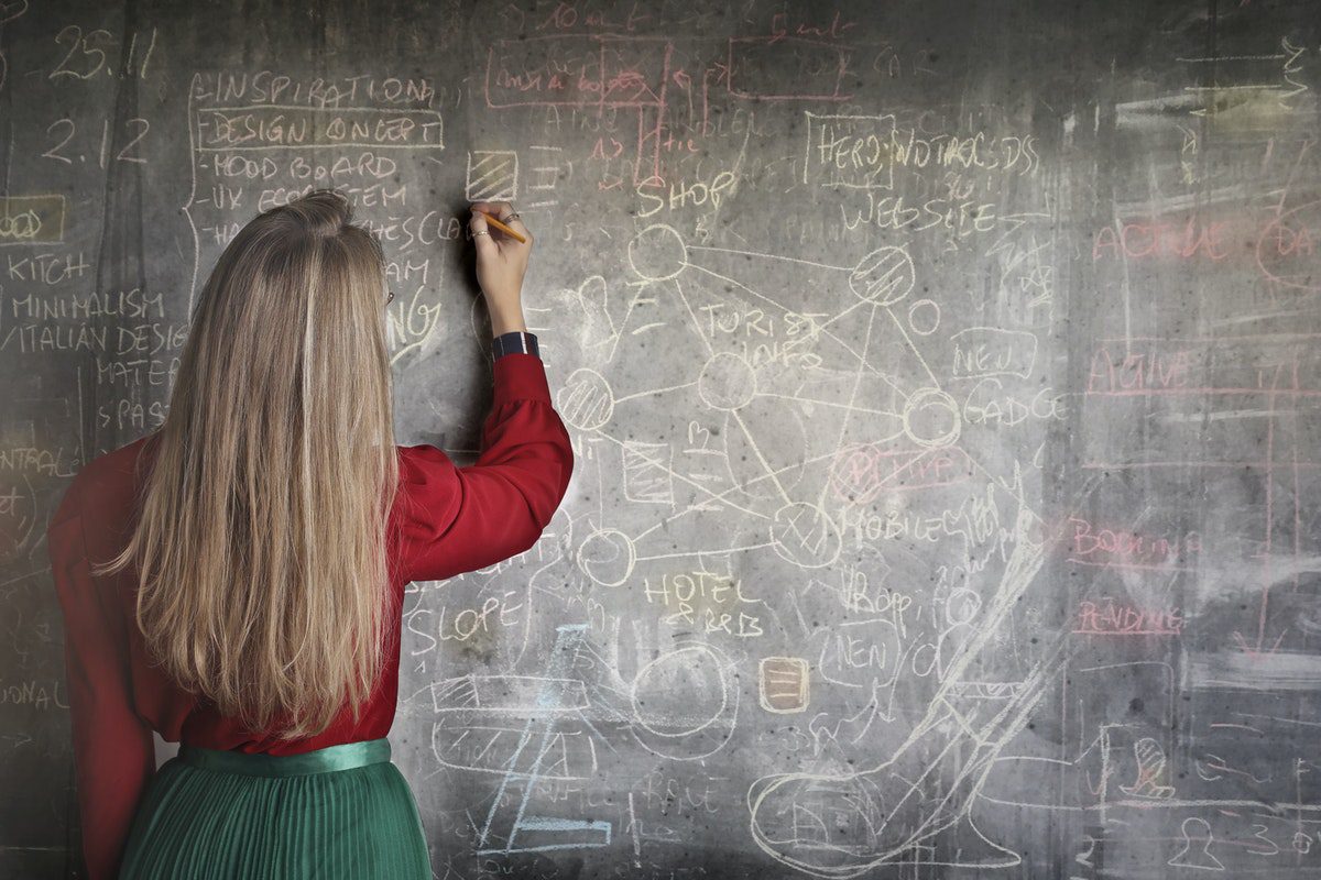A woman with a teaching license solving mathematical equations on a chalkboard and teaching undergraduate students.