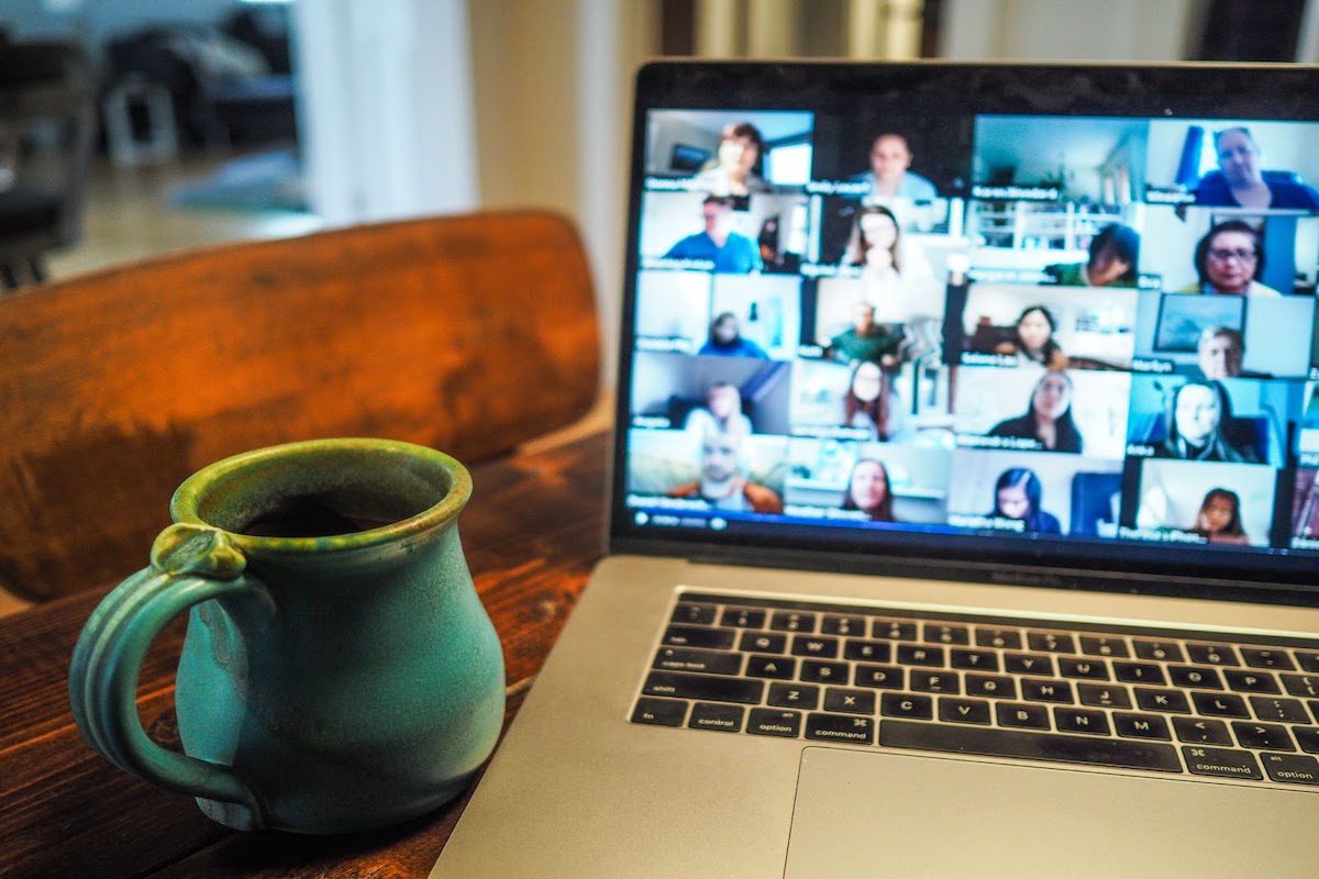A mug of coffee sitting next to an open laptop showing an online class with many students