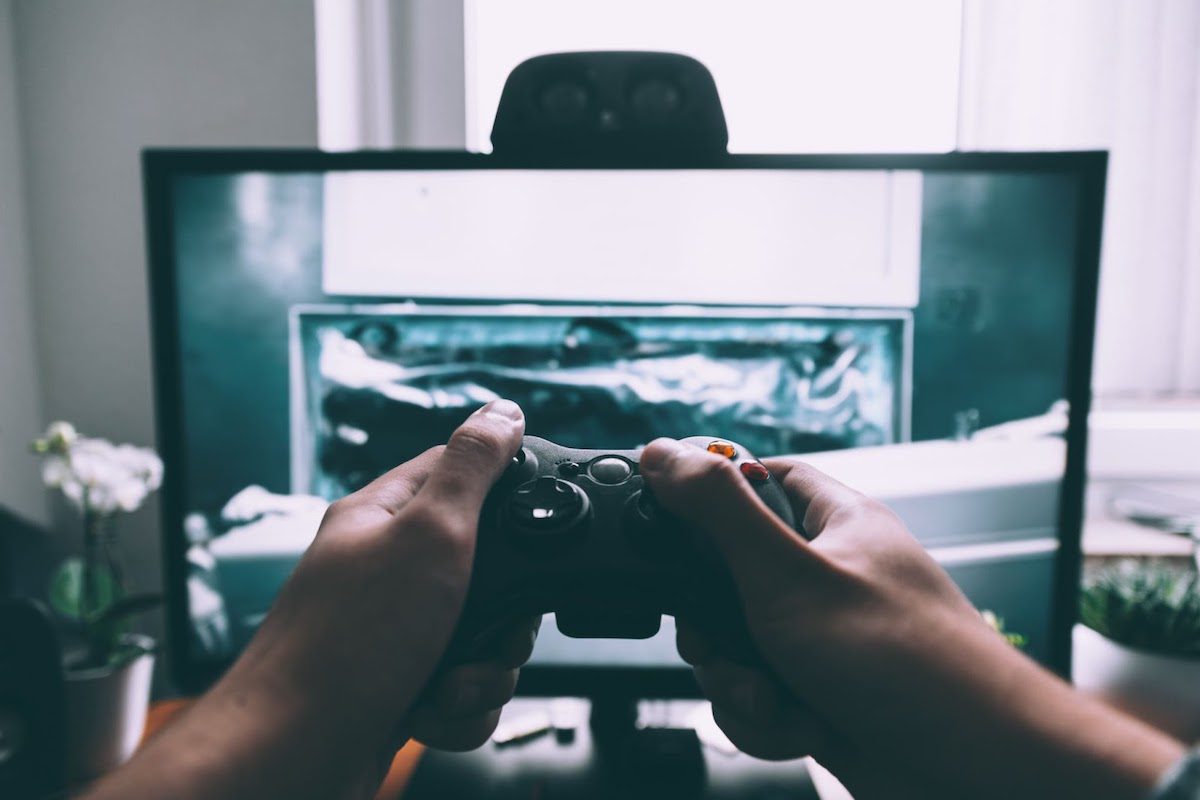 Hands holding a video game console controller in front of a monitor.