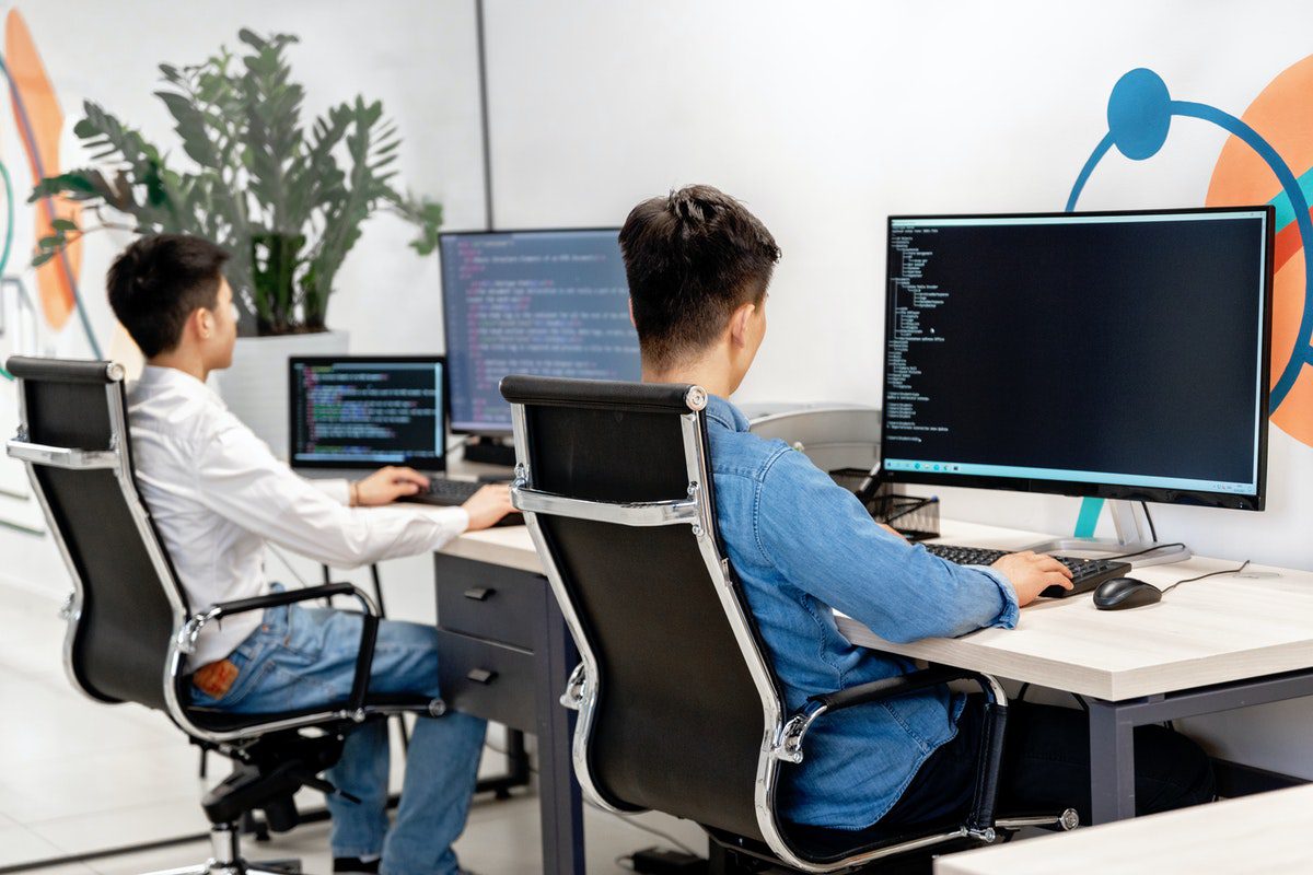 Two people sitting at a workstation looking at computers displaying coding programs
