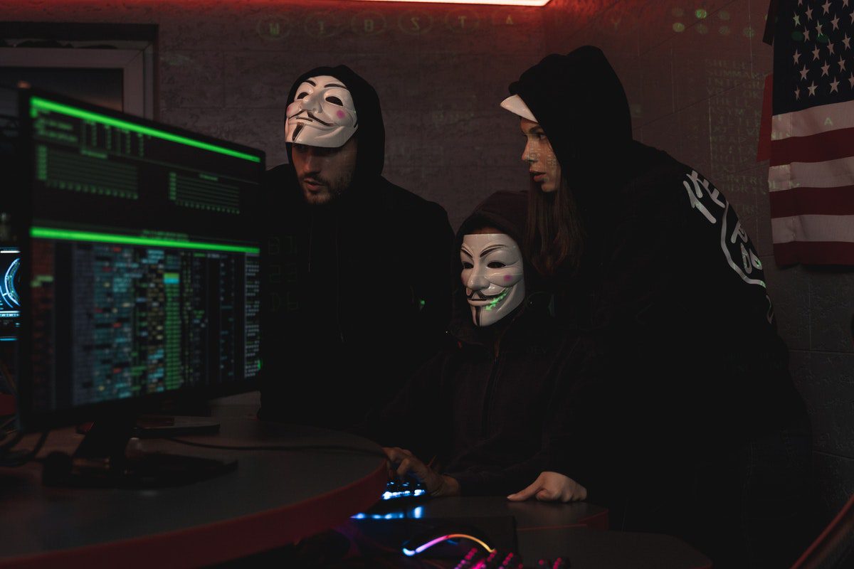 Three hackers in front of computers in masks and hoodies.